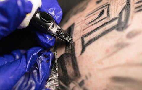 An image showing a closeup of the hand of a tattoo artist using a pen with black tattoo ink