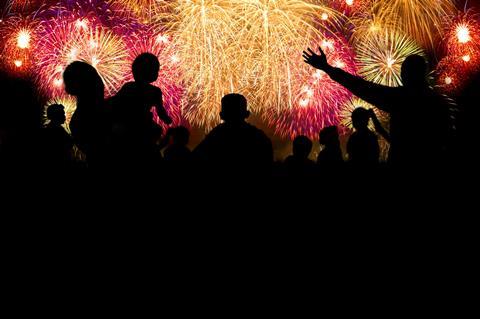 A photograph of a crowd of people watching a fireworks display