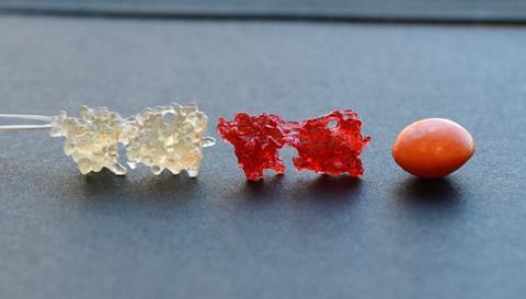An image showing two tiny blob-like shapes, one transparent, one red, next to an orange Skittles
