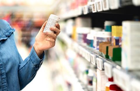 Person reading medication packaging by supermarket shelves