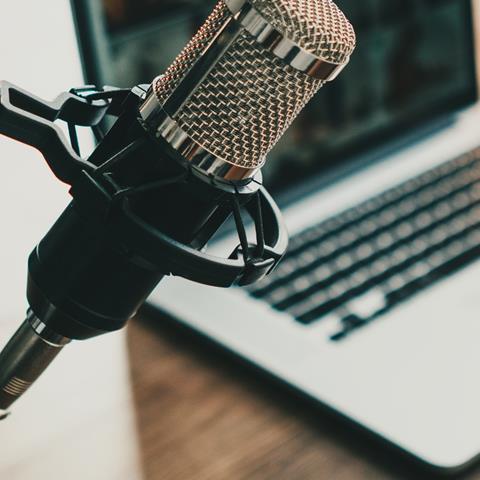 Close-up image of a microphone in front of a blurred-out aptop