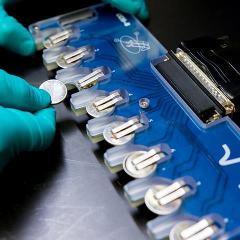 A row of coin batteries being tested by a scientist
