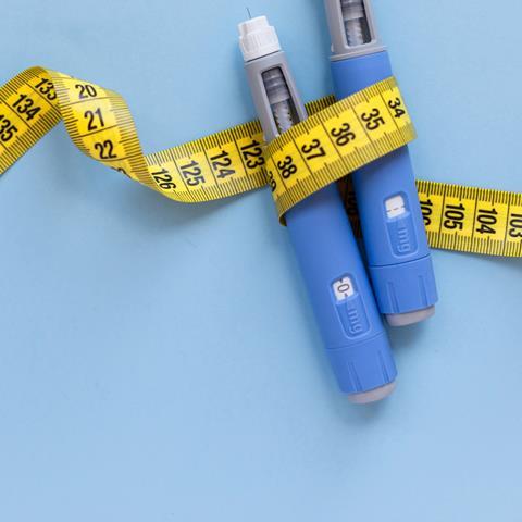 Front view in landscape format of two injector pens wrapped in a yellow tape measure