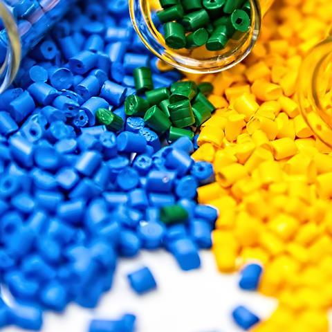 Close-up of chemistry vials or test-tubes containing thermoset plastic pellets in blue, green and yellow, spilling out onto the foreground