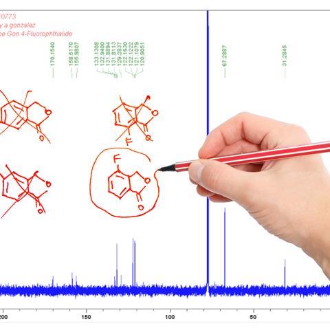 A printout of a carbon NMR spectrum. There are several different hand-drawn structures on one side, most of them crossed out. A hand holding a red pen is circling one of the structures