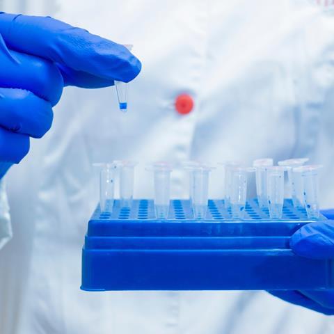Chemist holding a tray of vials in one hand, removing one vial from the tray with the other hand