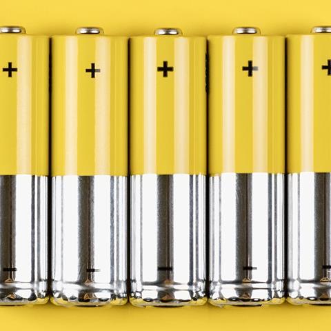Photo of five grey-yellow alkaline AA batteries on a yellow background.