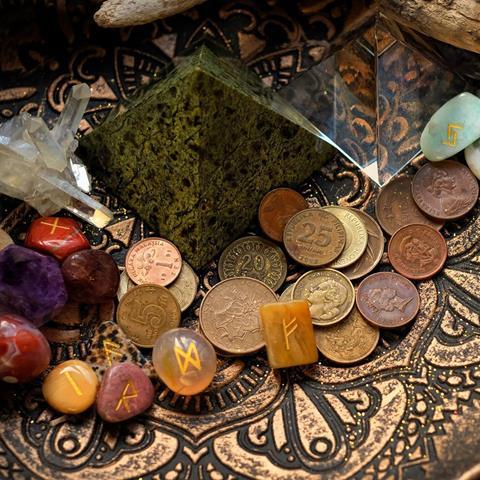 Looking into the contents of a black and gold patterned bowl containing a tree branch, diamonds and coins, alluding to witchcraft and potions