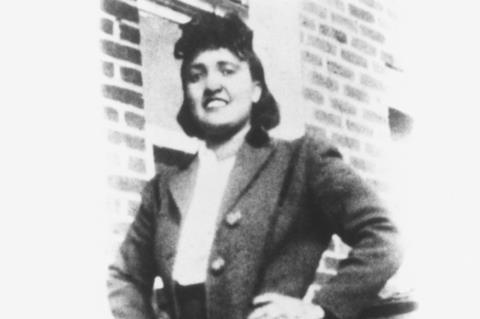 An old black and white photo of a young confident African American woman in fashionable 1950s dress