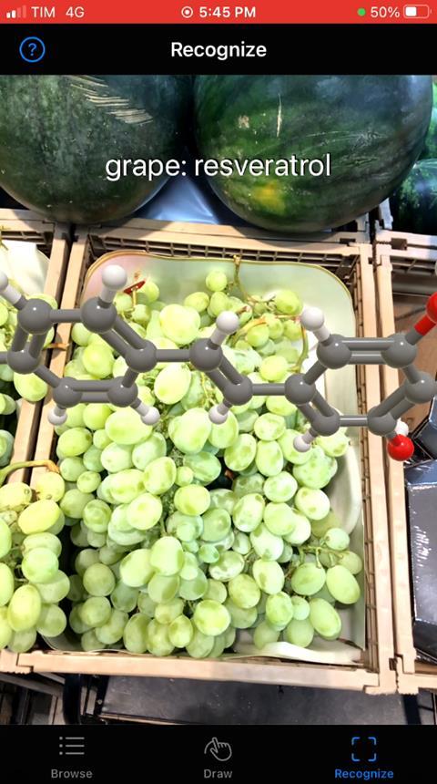 An image of a phone screen that shows grapes lying on a market stall table. On top of the grapes there's a 3D chemical structure of resveratrol