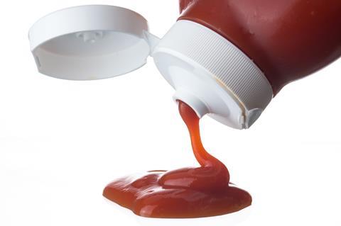 Image showing side view of a ketchup bottle squeezing out ketchup onto a flat white surface