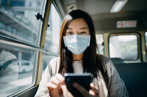 An image showing a woman with a mask checking her phone in a bus