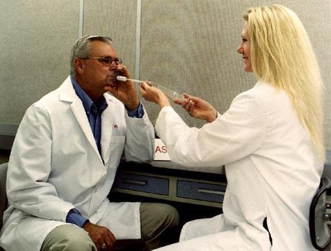 A photograph of George Aldrich sniffing a sample that is being dispensed by a colleague