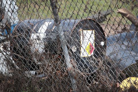 A drum labelled 'organic peroxide' that has been moved by bad weather and a flood resting against a chain link fence
