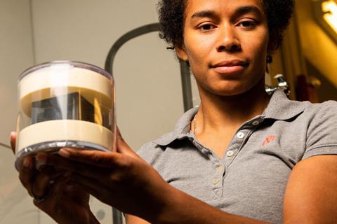 A woman holding a black cube in a perspex box