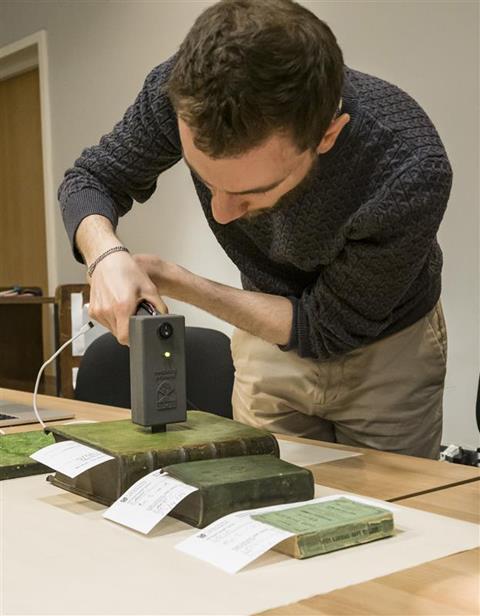 A researcher using a piece of technology to analyse some old books with green covers