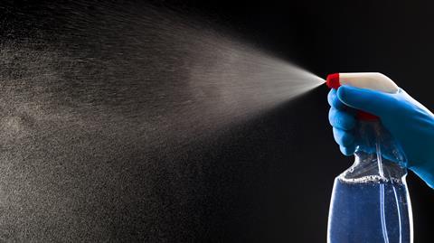 A photograph of a gloved hand spraying a chemical from a plastic bottle
