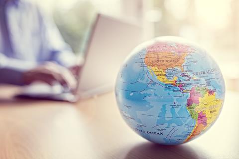 A globe map on a table in front of a man working on a laptop