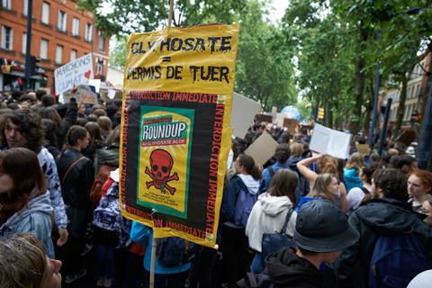 An image showing a protester holding a placard reading 'Glyphosate : license to kill'