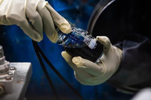 Hands in latex gloves with a bottle of dark blue liquid and two cables