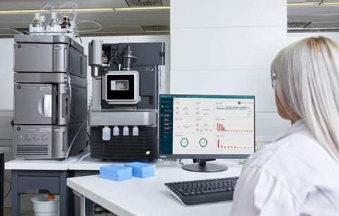 Scientist monitoring Waters Xevo TQ Absolute mass spectrometer and Acquity UPLC system with real-time data on a computer screen
