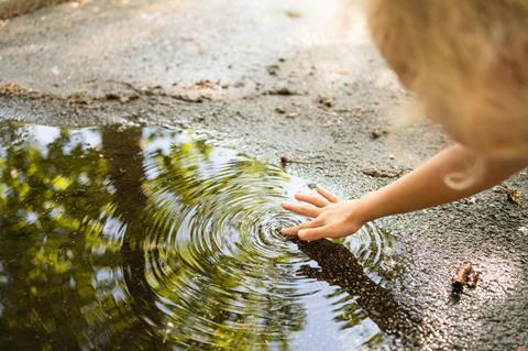 Child's hand touching water from a puddle