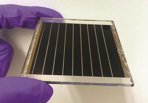 Close up of a hand in a purple latex glove holding a small solar cell