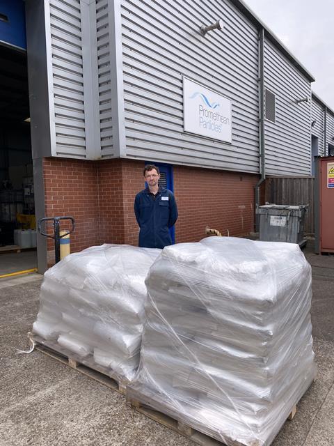 A man outside an industrial facility standing next to two pallets loaded with full sacks
