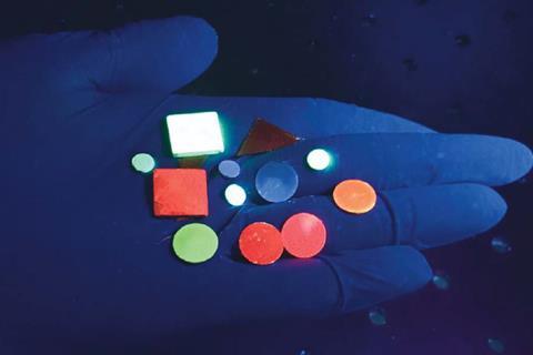 A photo of a number of small disks of a hard material sitting on a person's palm. Each of the disks glows in a different colour.