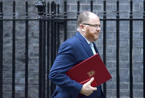 A profile shot of George Freeman, a middle-aged white man wearing glasses and a blue suit. He has a stern, concerned expression and is clutching a red leather book under his arm.