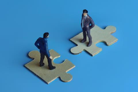 Two miniature figures in suits standing on jigsaw pieces