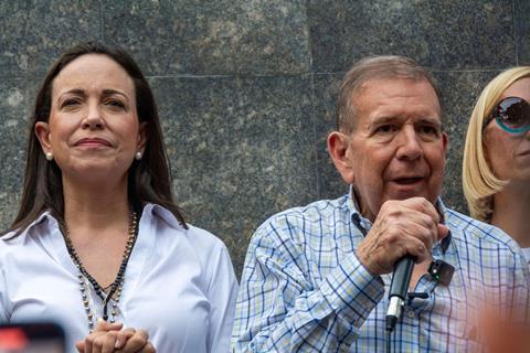 A woman stands next to a man who is talking into a microphone