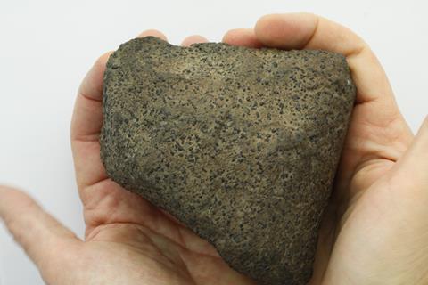 A photo of an unremarkable brown and black rock held in the palms of someone's hands