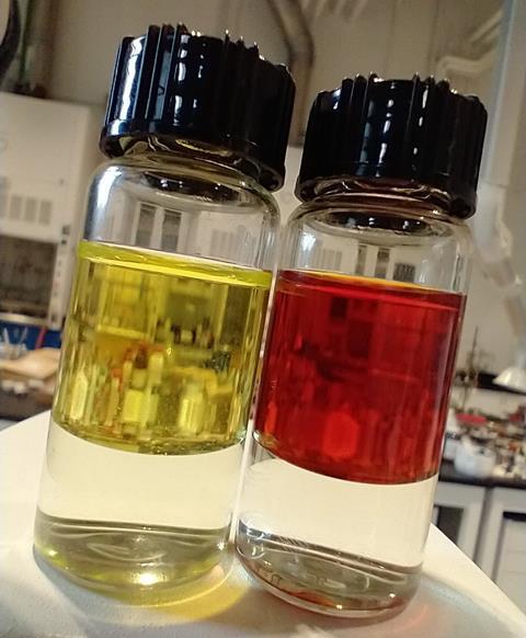 Two glass vials one contains a yellow liquid and the other contains a reddish brown liquid