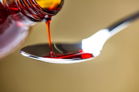 Red cough syrup being poured into a teaspoon