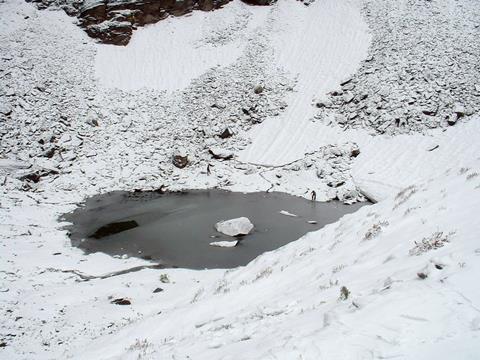 An image showing Roopkund Lake, with two people at the margins of the lake, giving a sense of scale