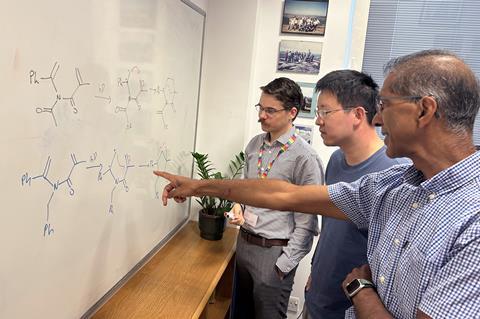 Three men discussing chemical structures drawn on a whiteboard