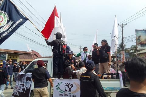A crowd gathered around a pick up truck of protesters with flags and a microphone in Indonesia