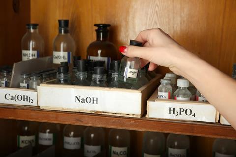 Hand picking up a Sodium Hydroxide NaOH bottle