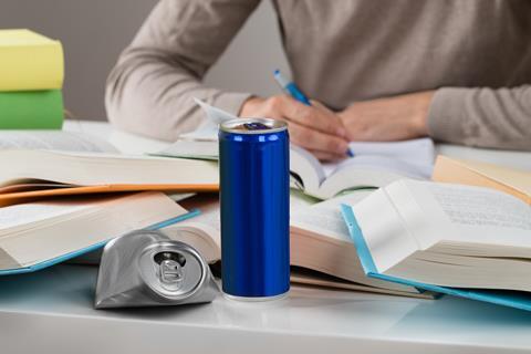male student studying with energy drinks and books at table 