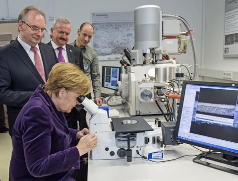 An image showing Angela Merkel using a microscope