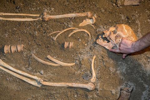 Human remains in sand being excavated by archaeologist