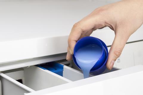 Closeup of a woman hand pouring liquid detergent in the washing machine