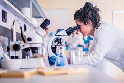 Researcher in lab coat using optical microscope