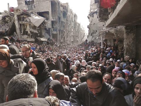 Residents wait in line to receive food aid distributed in the Yarmouk refugee camp in Damascus, Syria