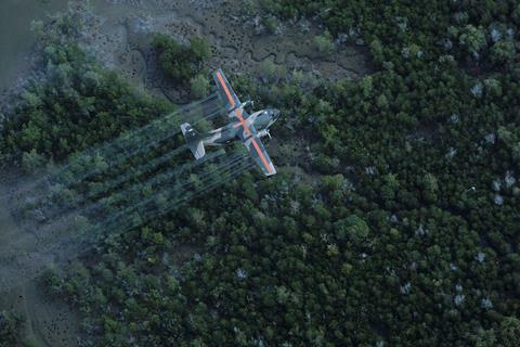 A military plane spraying liquid over a forested area