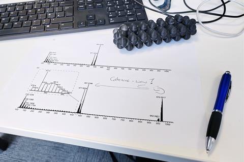 An office desk with a computer keyboard and a mass spec results printed on a piece of paper where someone has written Catenane WOW!