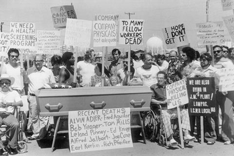 A group of asbestos workers line up by a coffin in protest