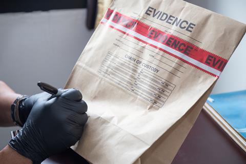 forensic 's hand in black glove writing on evidence bag and seal by red tape in crime scene investigation