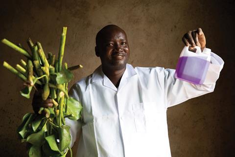 An image showing Richard Arwa holding weeds and fuel extracted from them